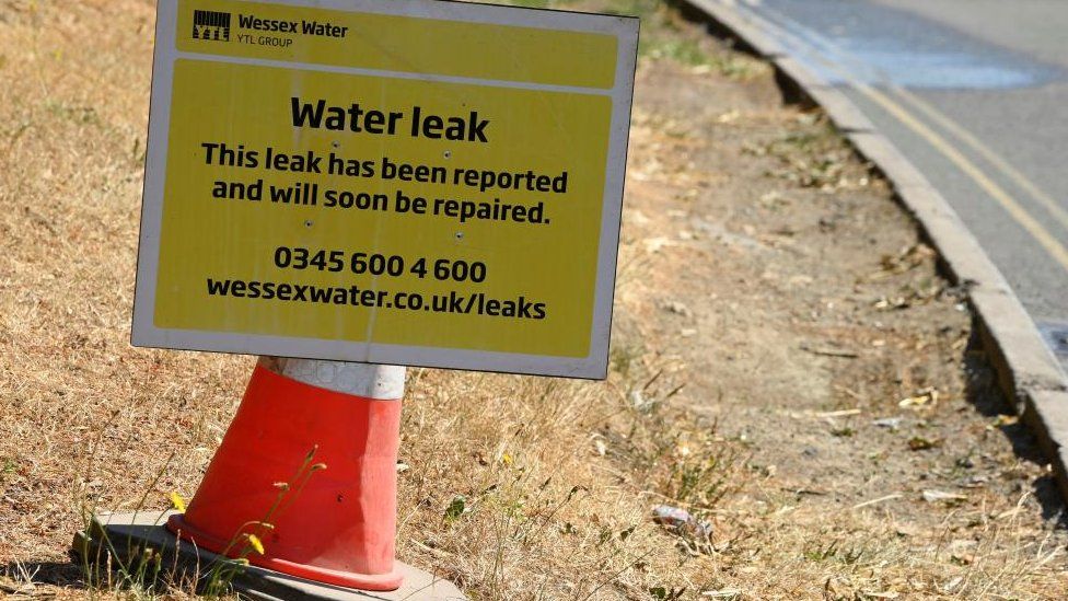 A sign from a water utility company is placed near a roadside water leak in Bradford-on-Avon
