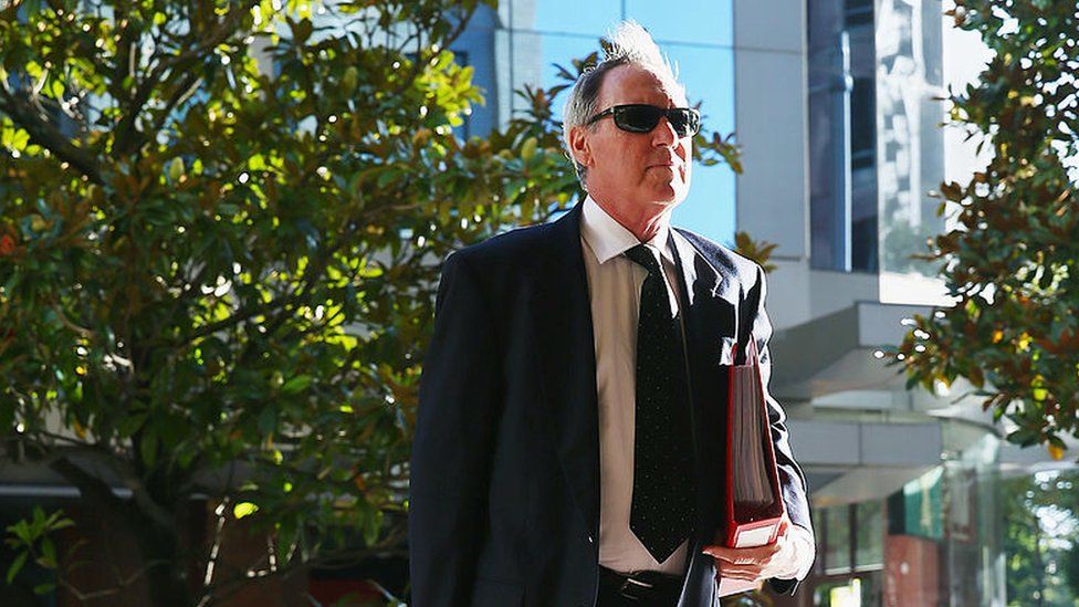 Robert Hughes holding a binder outside court in Australia