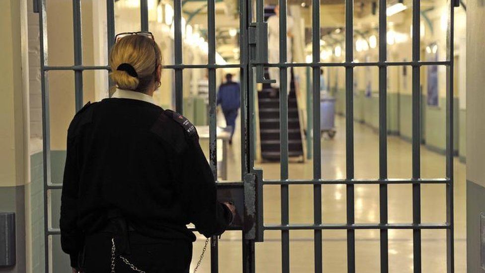 Prison officer stands behind gate