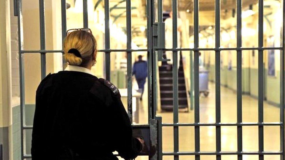 A prison officer looking through a secure gate inside a prison