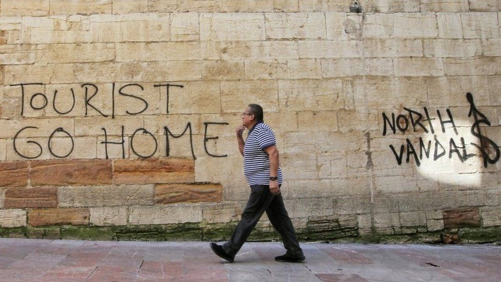A man walks past a "Tourists Go Home" graffitti on a wall close to the City Hall in Oviedo, northern Spain,