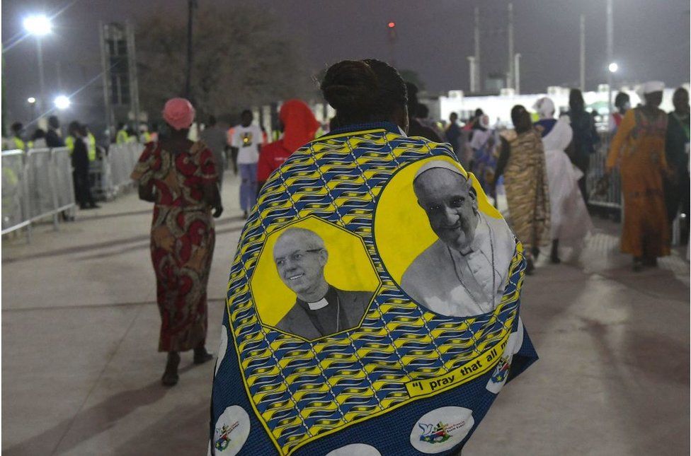 Woman walking with a shawl with pictures of Pope Francis and Justin Welby on it.