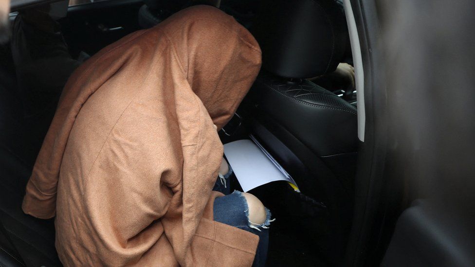 The arrested woman sits in the police car covered by a blanket