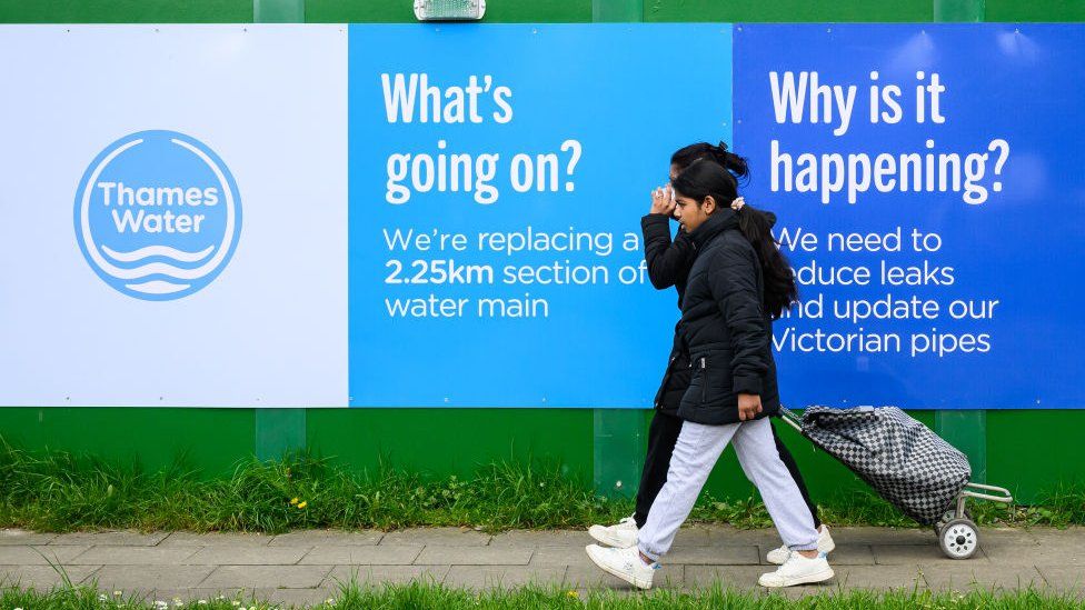 People walking past Thames Water sign
