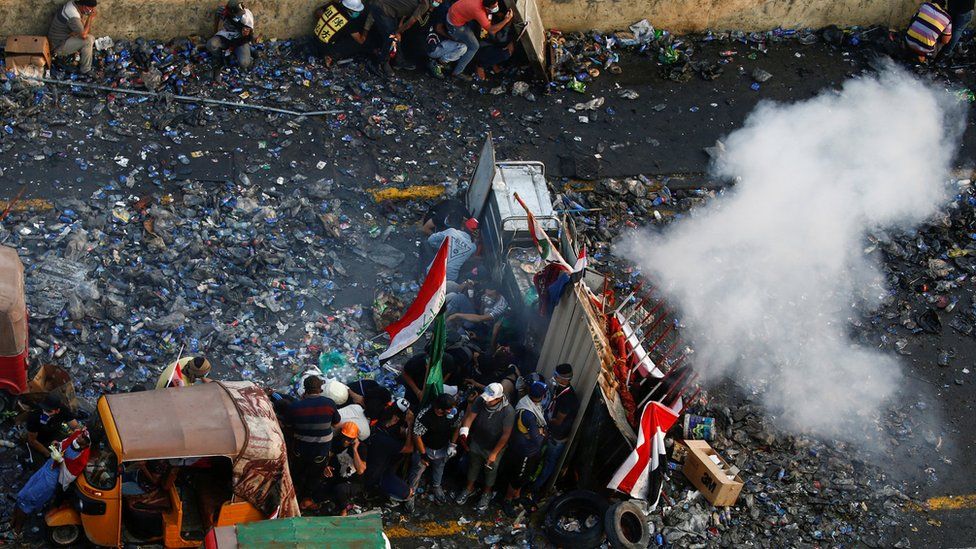 Anti-government protesters take cover from a tear-gas canister during a protest in Tahrir Square, Baghdad (28 October 2019)