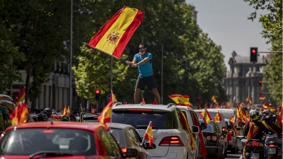 Image shows a man waves a Spanish flag as he takes part in an in-vehicle protest