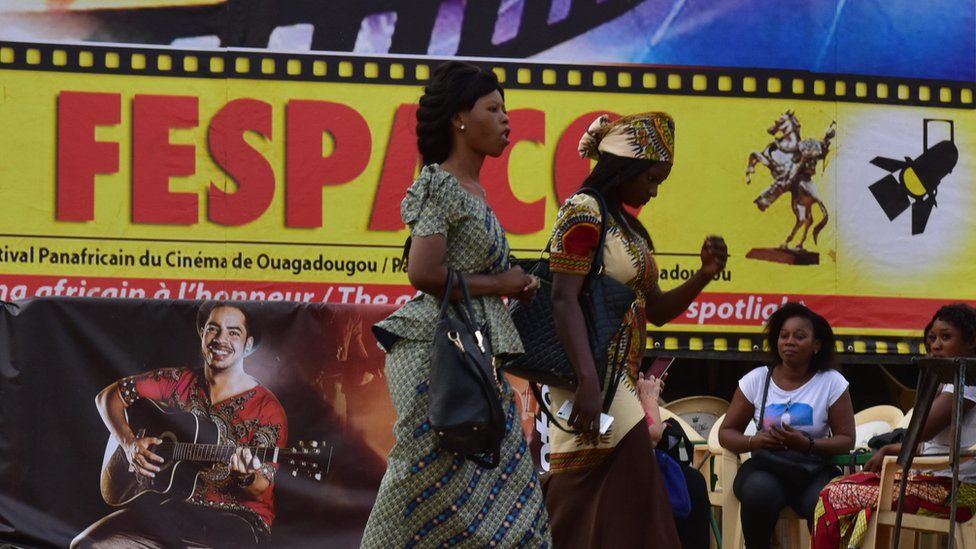 Festival-goers walk past an official poster of the Fespaco