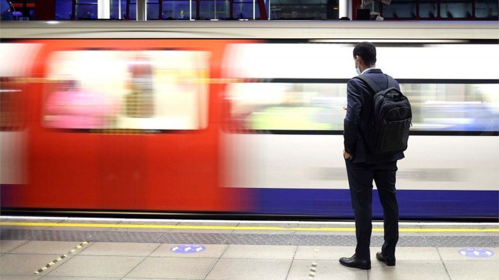 Man stands on a platform while a Tube train goes past
