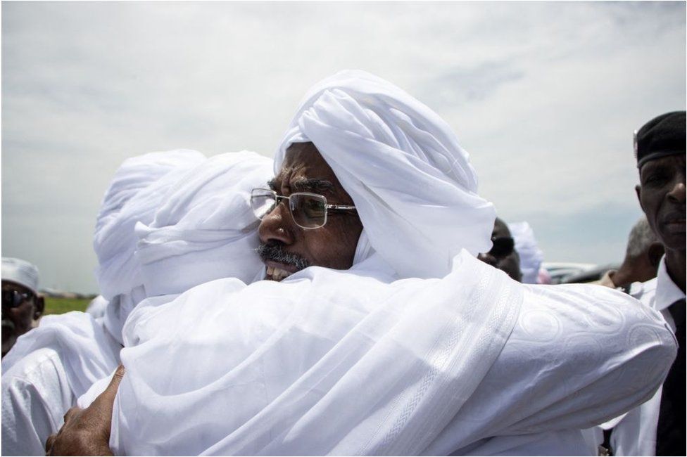 Two men dressed in white traditional clothes embracing.