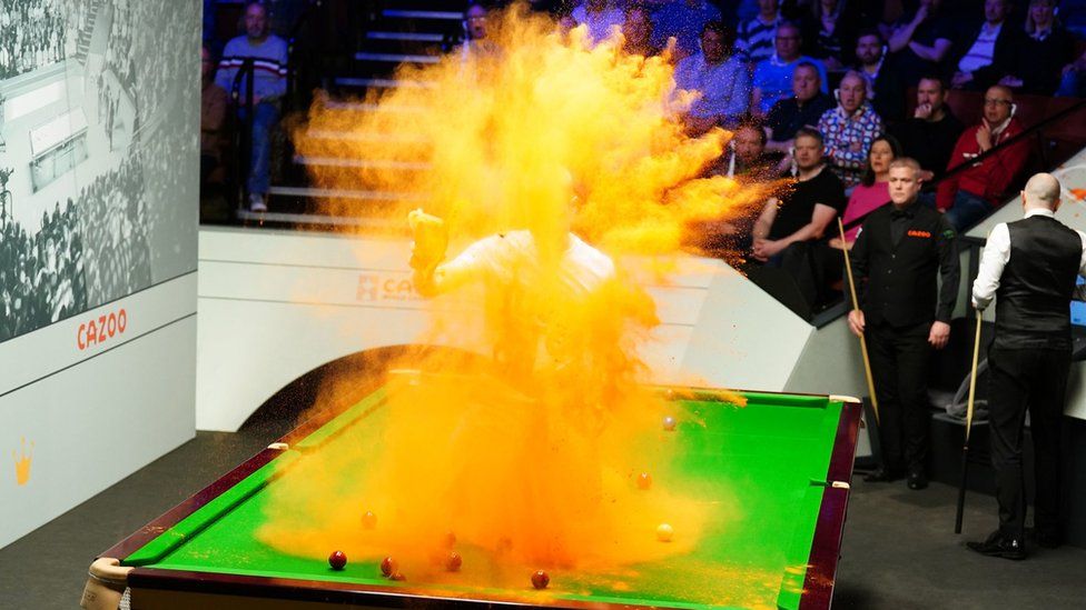 Ein Demonstrant wirft Sand in die Luft, während er bei der Snooker-Weltmeisterschaft an Tisch eins sitzt