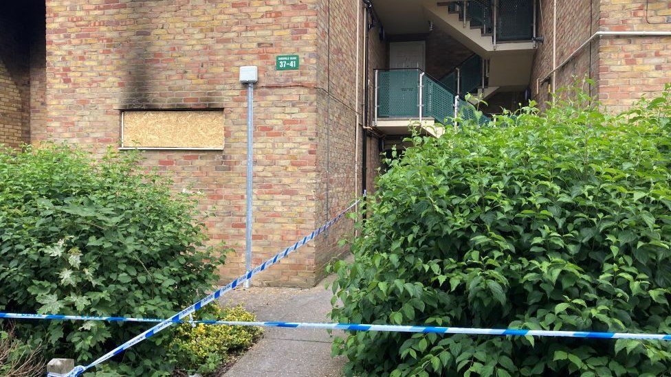 The property in King's Hedges with boarded up windows and black smoke damage. Police tape is at the front of the flats.