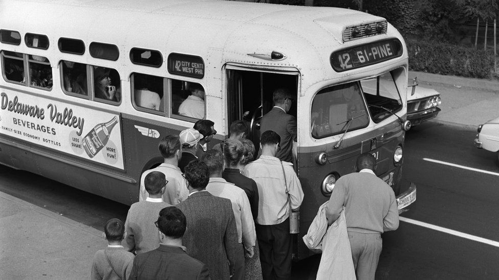 Line of commuters stepping into crowded public transit bus in the 1950s