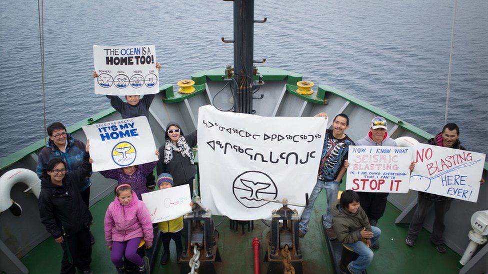 Clyde River residents hold up anti-seismic blasting signs on the bow of the Arctic Sunrise, during a ship tour