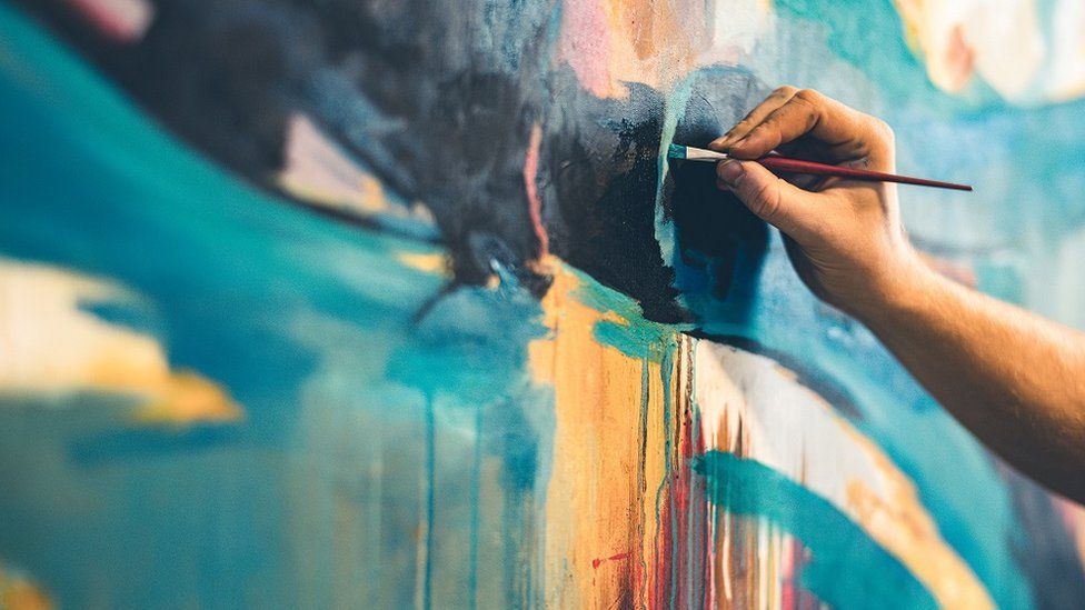 An artist's hand with paintbrush painting a picture
