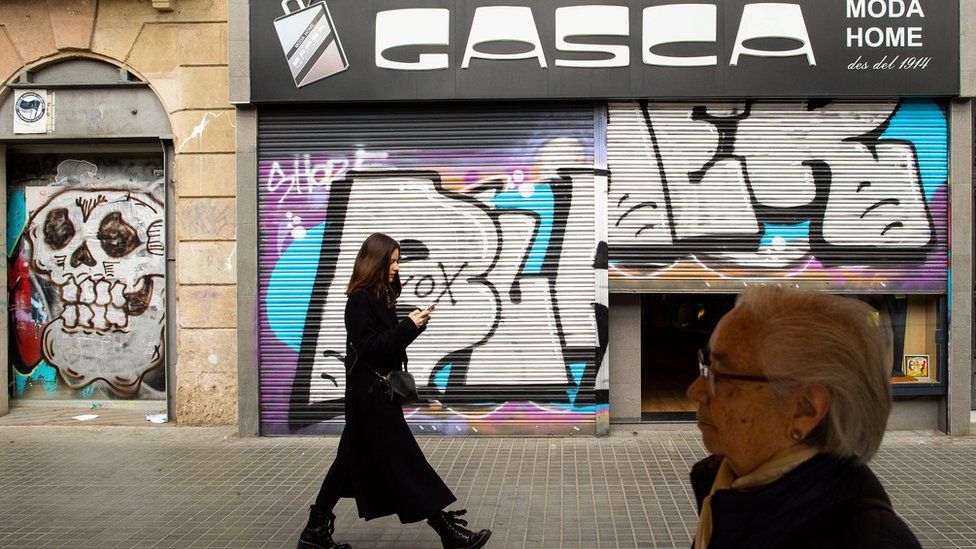 Members of the public walk past a closed shop as new measures against the coronavirus expansion are implemented on March 14, 2020 in Barcelona, Spain.