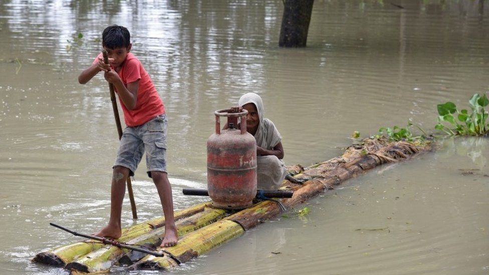 A boy ferries a woman and gas canister across floodwater in Assam, India (18 Aug 2017)