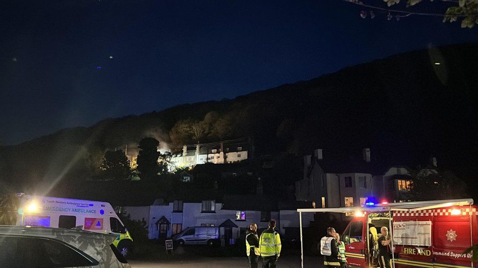 Ambulance and fire personnel standing together while the cottages burn in the distance