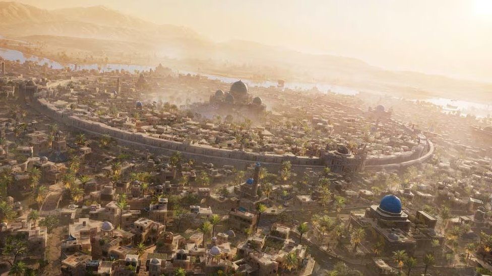 A wide, aerial view of Baghdad as seen in Assassin's Creed Mirage. It shows a circular wall around the city, which has a large building with a giant dome on top, and four smaller domes on each corner. The city is tightly packed with many flat-topped buildings. As the scene recedes the landscape fades away into desert, and a cloud of sand obscures the background.