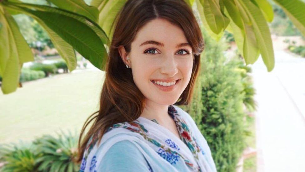 Photograph of Hailey smiling with green leafy background