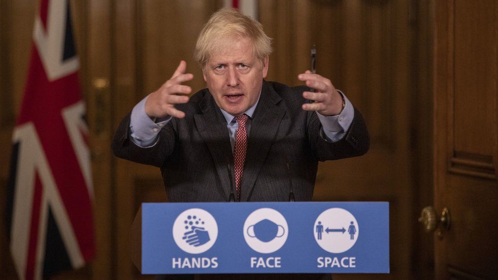 Boris Johnson speaks at the podium for a No 10 press office - it reads 'Hands. Face. Space'. He is gesturing with his arms up