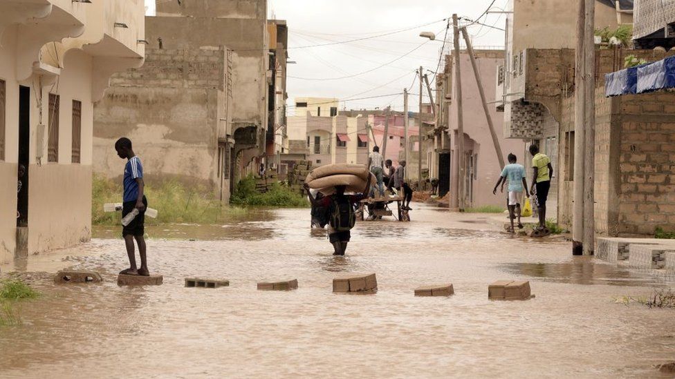 A man carries a mattress on his head while walking in flood water in the Keurs Massar area in Dakar on September 7, 2020 after heavy rains in Senegal.