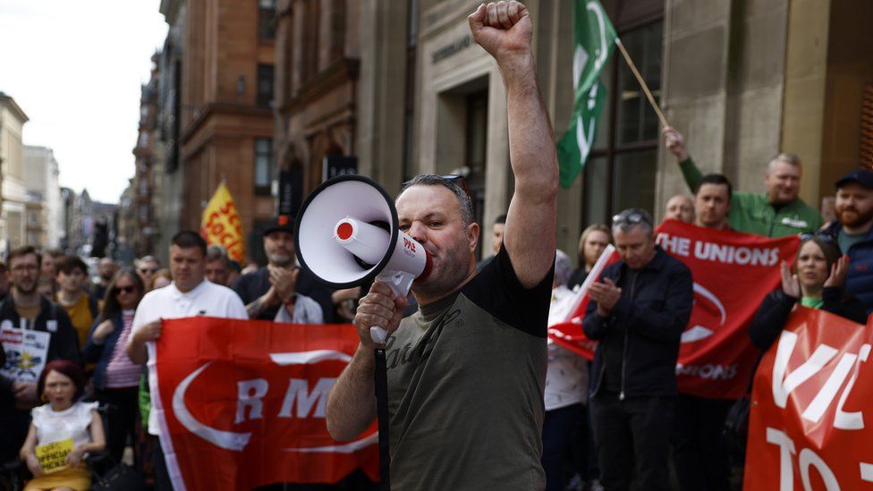 An RMT union member on a strike picket line with his fist in the air holding a megaphone