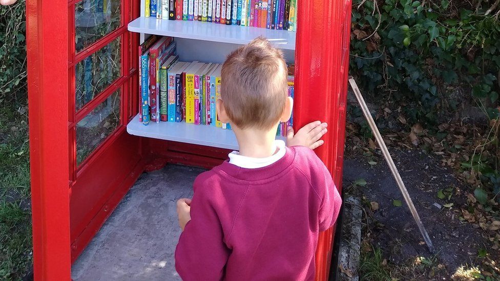 Child looking at books in a red phone box