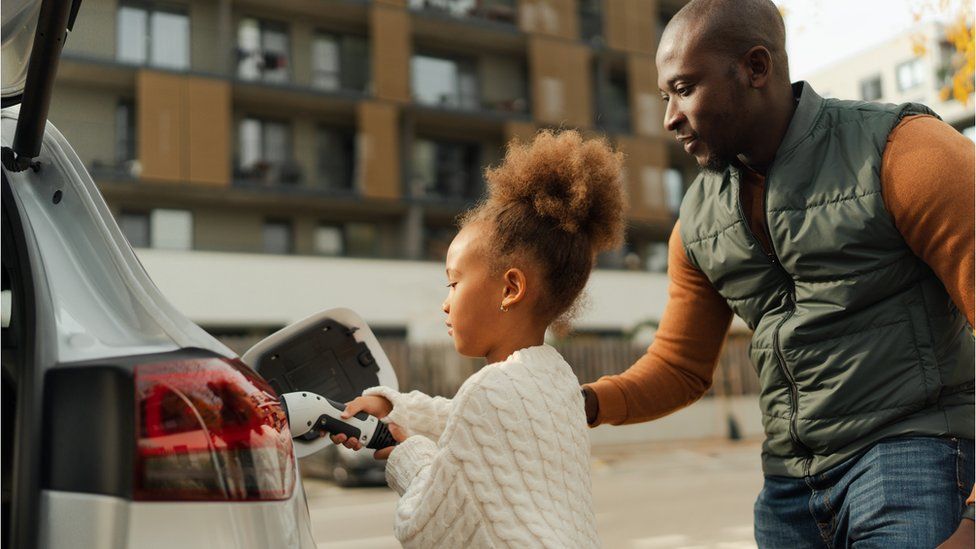 Close-up of father with his daughter charging their electric car during autumn day