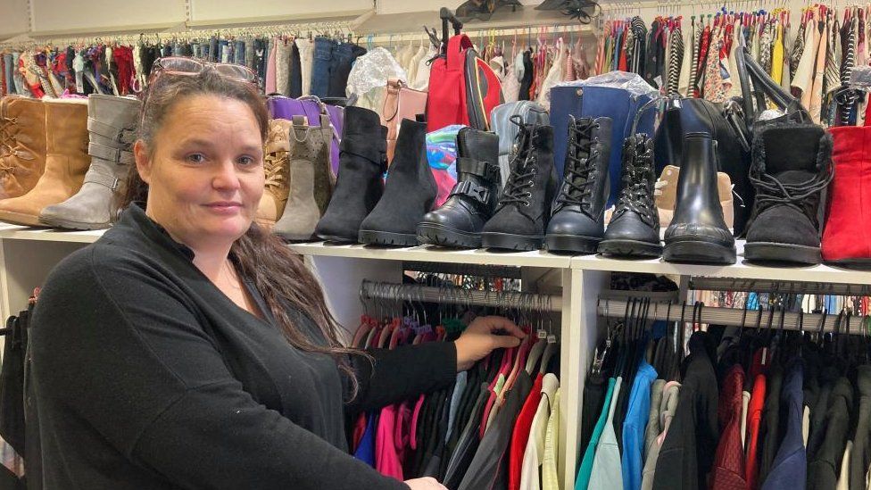 Woman wearing black top stands next to rails of shoes and clothes