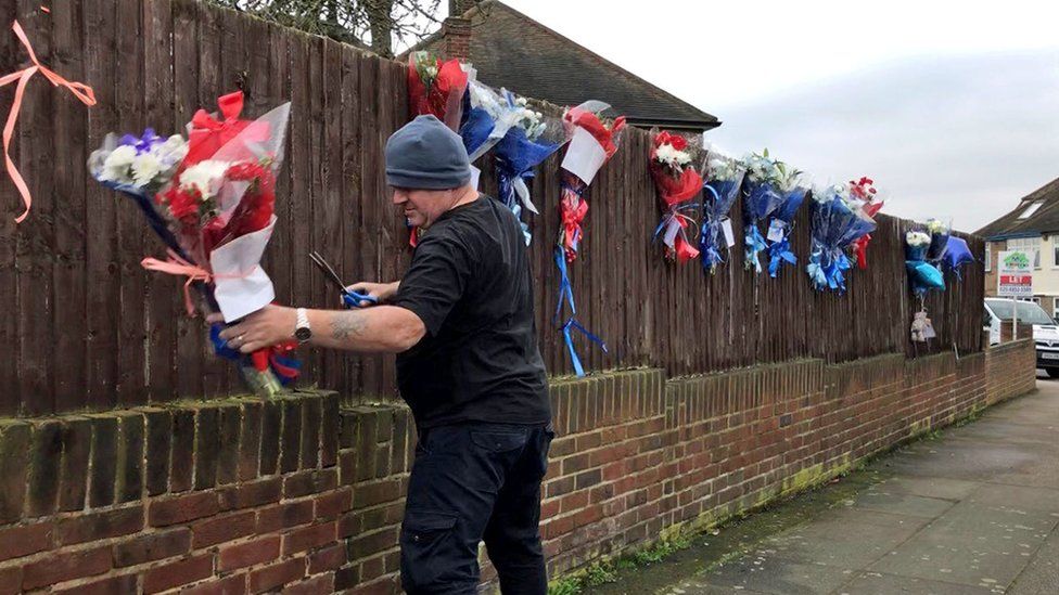 A man removes floral tributes from a fence on South Park Crescent