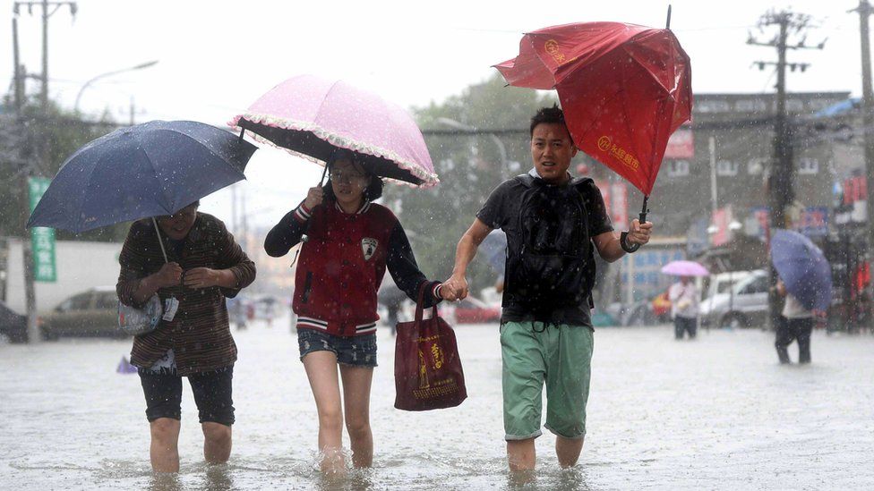 People walk through a flooded street in Beijing on July 20, 2016.