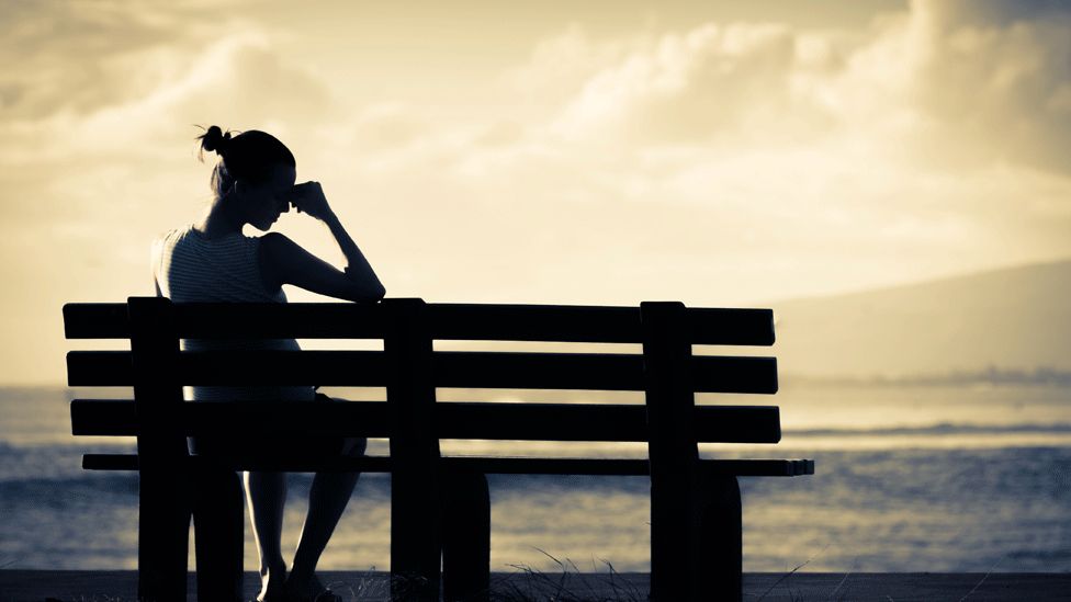 Woman sitting with head in hands on a park bench