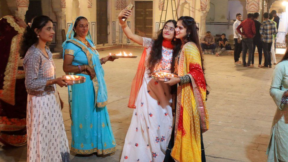 2021 年 11 月 4 日，星期四，在印度拉贾斯坦邦斋浦尔的历史悠久的 Ramchandra Ji 寺庙，排灯节期间，女孩们在点亮土灯“diyas”后自拍。