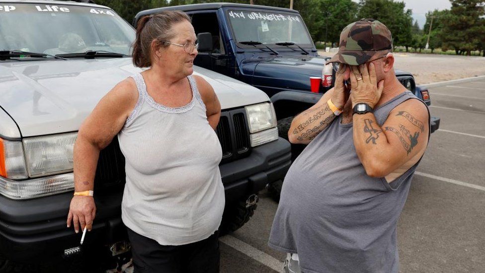 Dawn Butterfield and Robert Butterfield from Yreka, who have evacuated the area amidst the fast-moving McKinney Fire, stand near some car outside an evacuation shelter in Weed, California