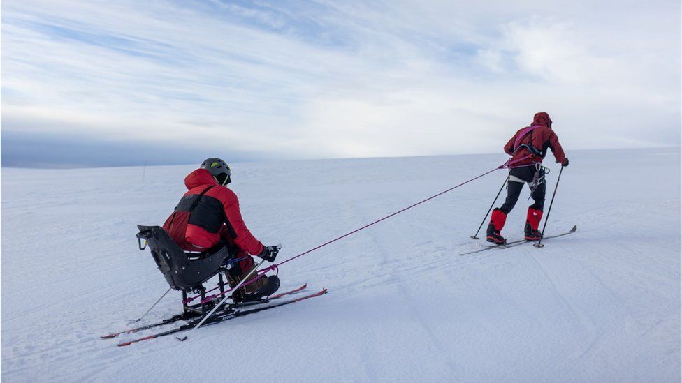 Niall McCann skiing, tied to Darren Edwards who is on a sit ski. They are tied together by a rope