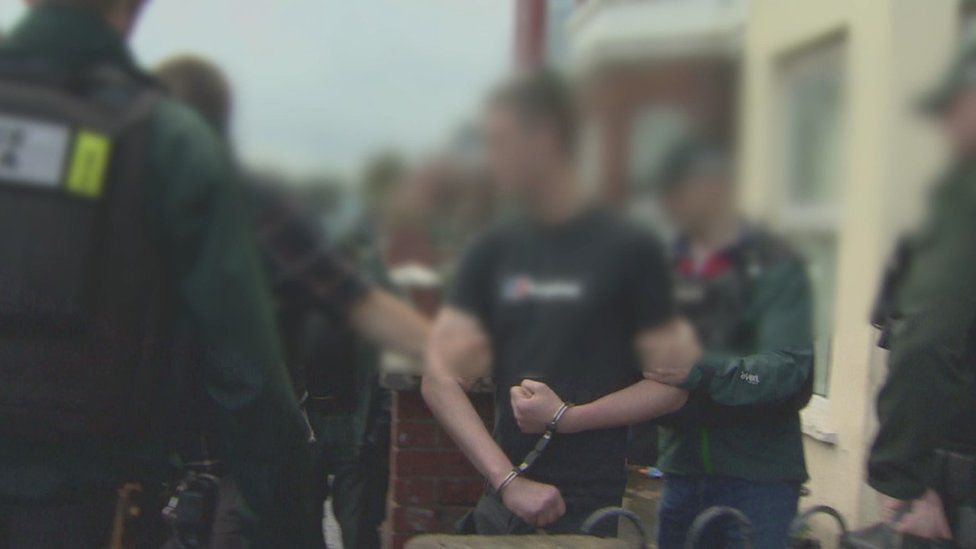 A blurred shot of police officers arresting a man in a black T-shirt