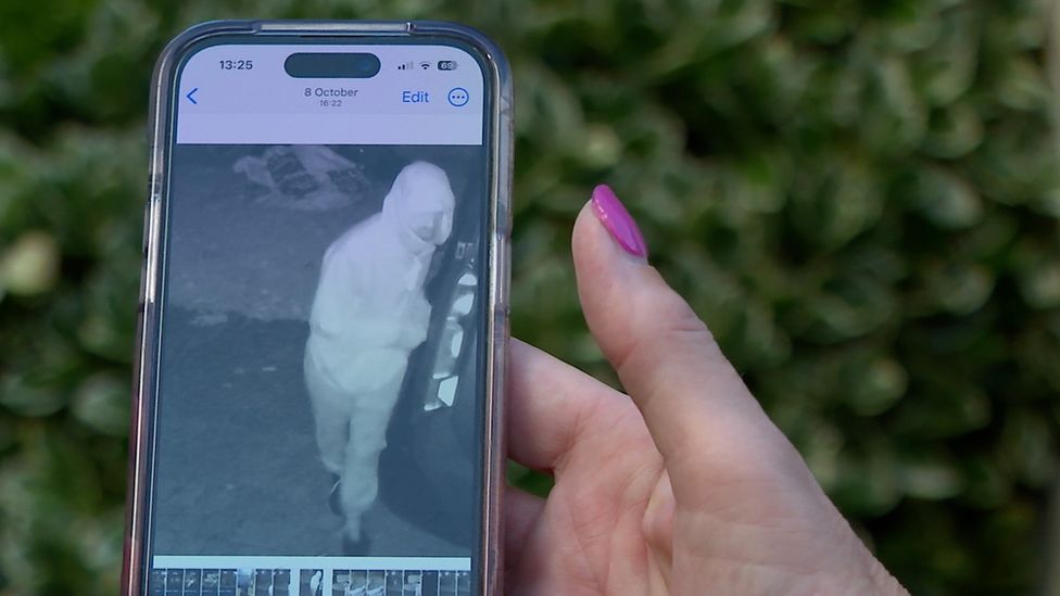 A mobile phone in a woman's hand showing a picture of a burglar