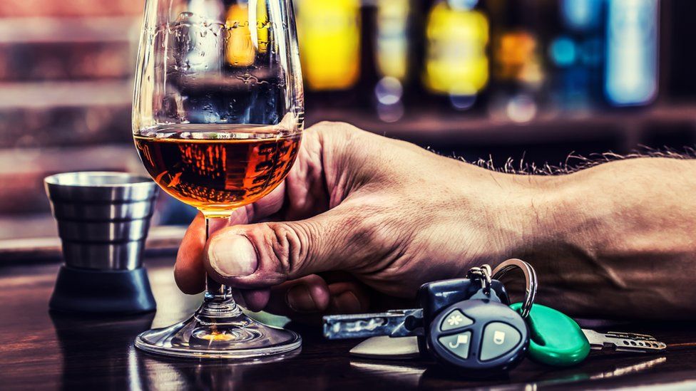 Glass of spirits being held by male hand with car keys on bar counter