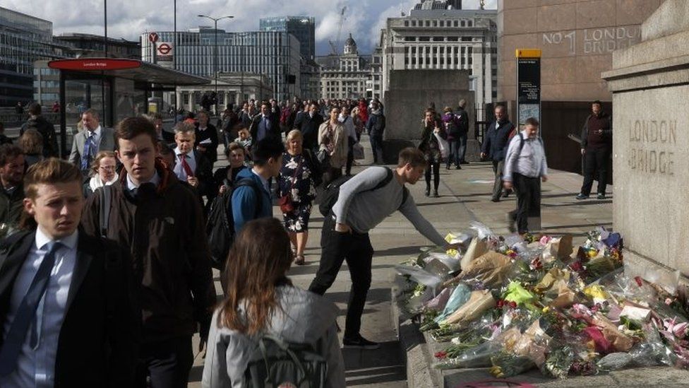 A man places flowers as commuters walk past flowers and messages for the victims of the London attacks as they cross London Bridge (06 June 2017)