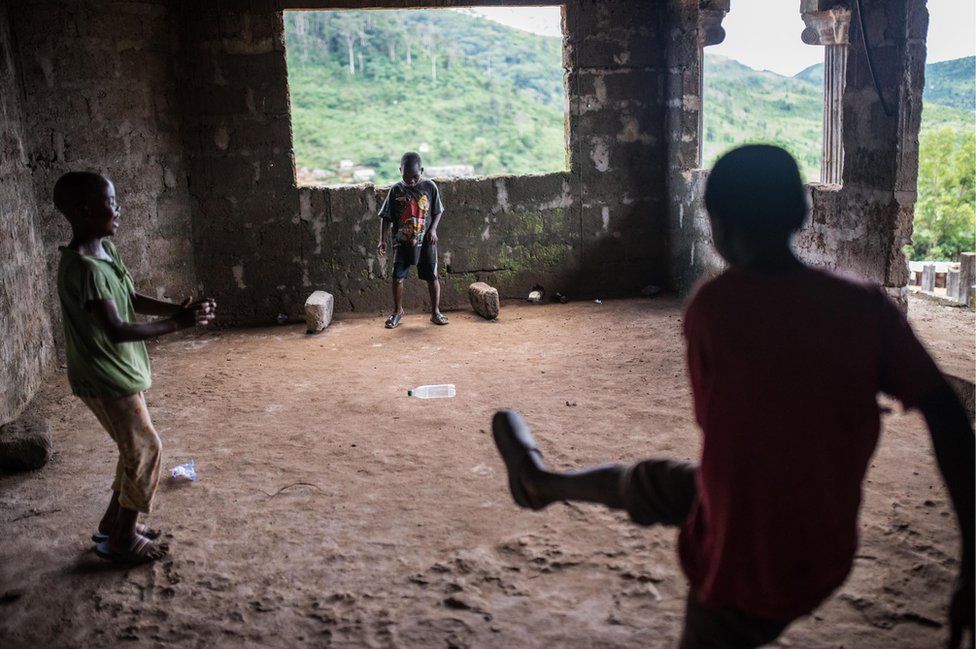 Boys play football with a plastic bottle in a back room of the house