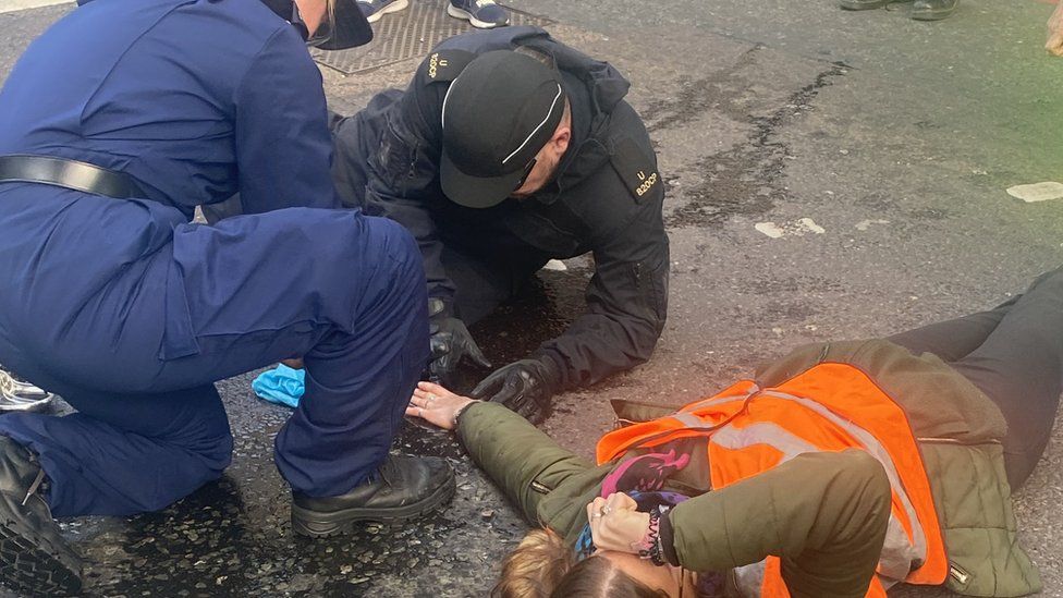 Public Order Instructors from the Metropolitan Police work to release a woman who has glued herself to the floor at an Insulate Britain protest on Bishopsgate,