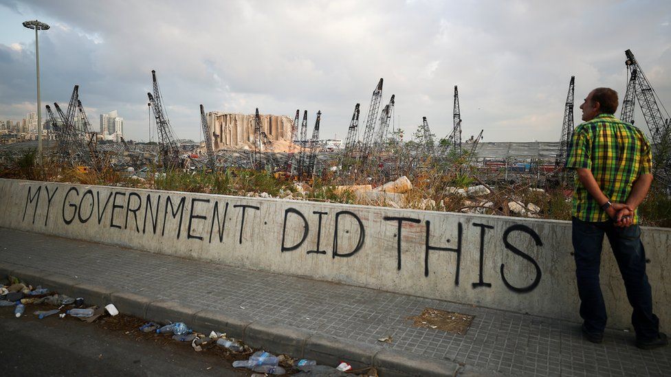 A man stands next to graffiti saying "my government did this", near Beirut's damaged port (11 August 2020)