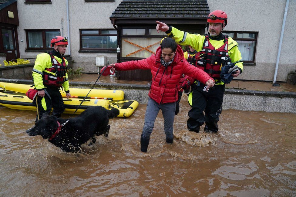 Members of the emergency services help a woman in Brechin, Scotland, as Storm Babet batters the country.