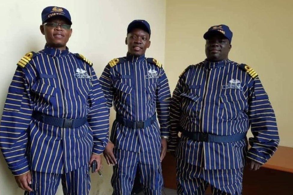 Three customs officers stand next to each other in their new, blue-and-white striped uniforms.