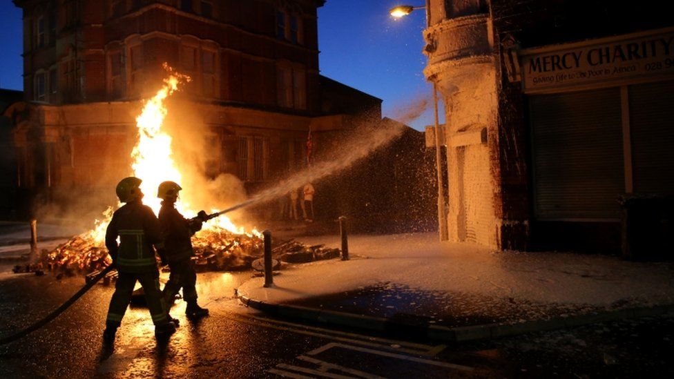 Firefighters douse nearby buildings as a bonfire is lit in Albertbridge Road, Belfast ahead of the key date in the protestant loyal order marching season - the Twelfth of July