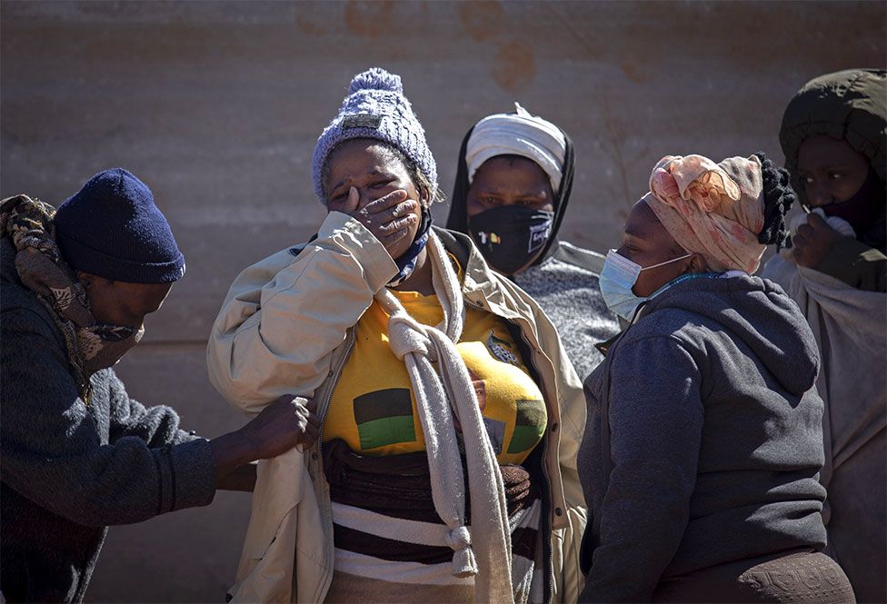 Relatives of a deceased looter mourn next to his body after he looted goods from shops in the area, Johannesburg, South Africa, on 13 July 2021