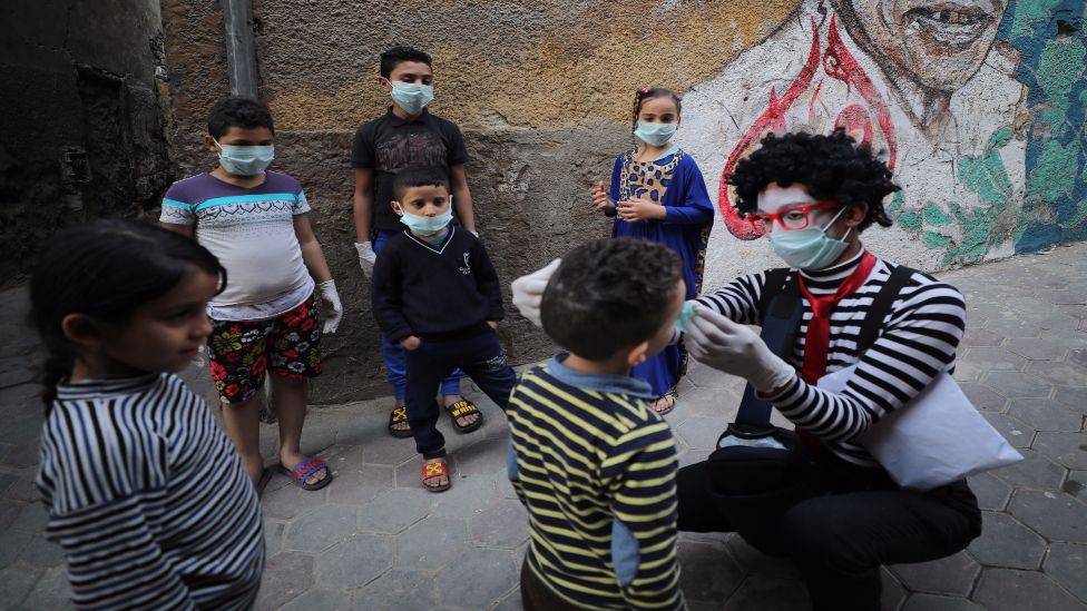 Egyptian clown Ahmed Naser wearing a face mask helps children to put on face masks