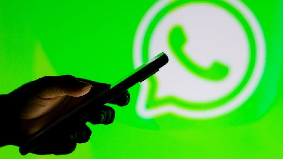 Person holds a smartphone against a WhatsApp logo background