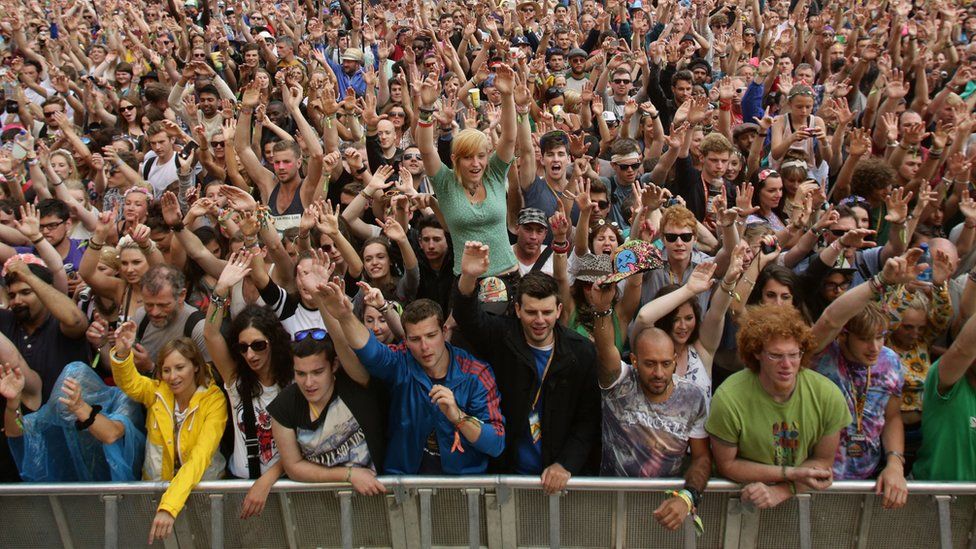 Сотни любителей музыки перед фестивальной толпой. В солнечный день царит праздничная атмосфера, и почти все держат руки в воздухе с радостным выражением лица.