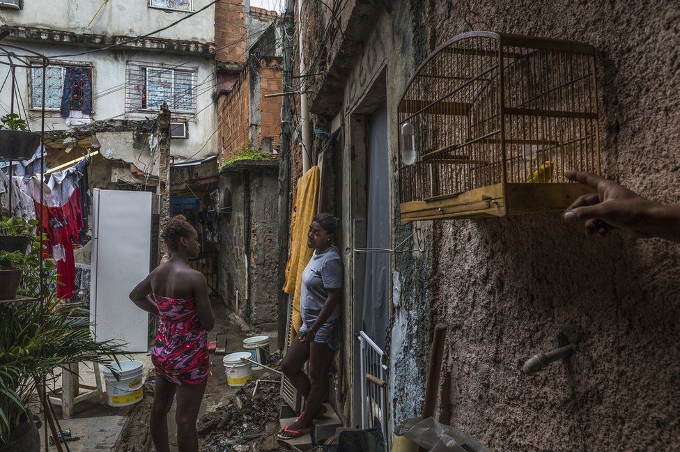 Women waiting in one of the alleyways while they fill up their water buckets. Favela Vila do Metro community, Mangueira, Rio de Janeiro, Brazil